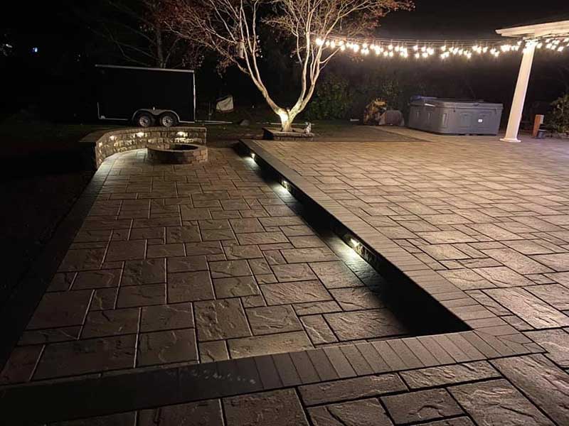 Interlocking Paver Patio, Fire Pit and Retaining Wall at night time with landscape lighting